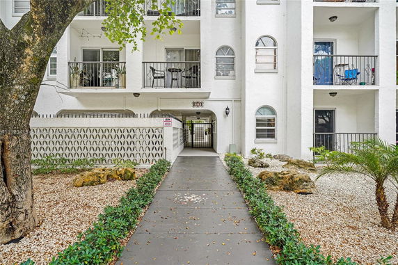 Elevated facade of a white multi-story building with balconies and an entrance pathway.