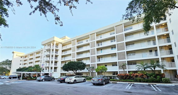 Front view of a multi-story residential building with balconies and a parking area in front.
