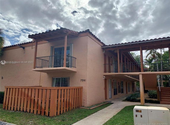 Front view of a two-story building with balconies and a wooden fence.