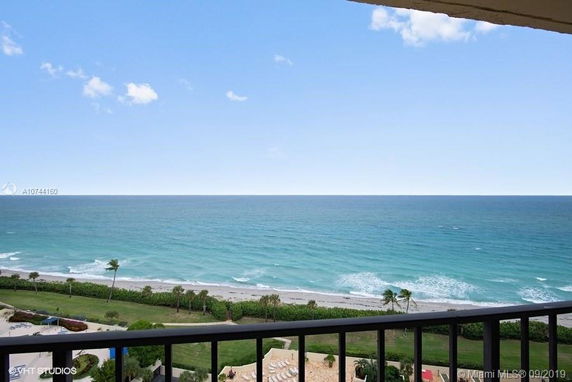 Panoramic view of the ocean from a balcony with a sandy beach and green landscaping below.