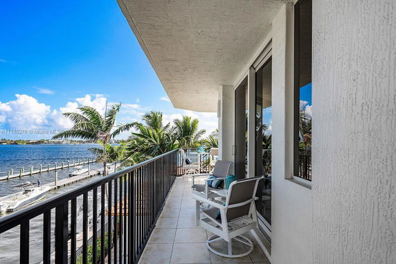 Outdoor balcony view overlooking a waterfront with boats and palm trees.