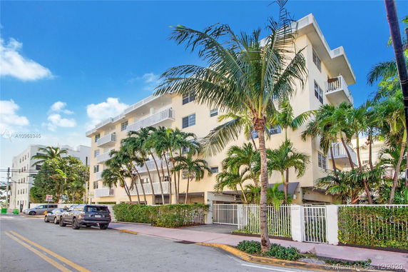 Front view of a multi-story residential building with balconies and palm trees.