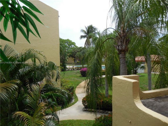 View of a garden area with palm trees and pathways near a beige building.