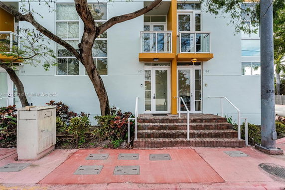Front view of a modern building entrance with small balconies and steps leading to doors.