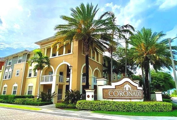 Front view of a multi-story residential building with palm trees and a sign reading 'Coronado'.