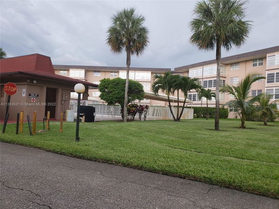 View of a multi-story building with a lawn and palm trees surrounding it.