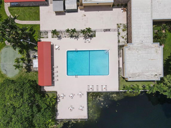 Aerial view of a swimming pool with surrounding seating and nearby structures.