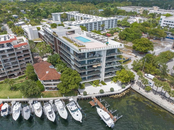 Aerial view of a multi-story residential building near a waterfront with boats docked.