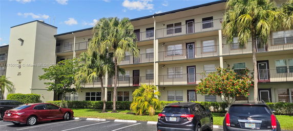 Front view of a multi-story residential building with balconies and parked cars.