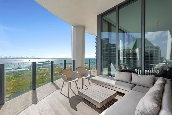 Outdoor balcony with glass railing and seating area, offering a panoramic view of the sea and cityscape.
