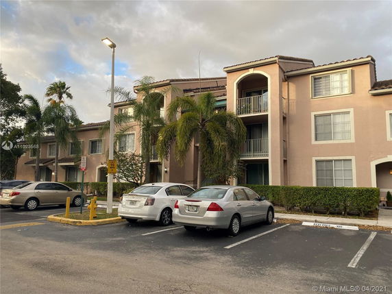 Front view of a multi-story residential building with parking spaces and several parked cars in front.