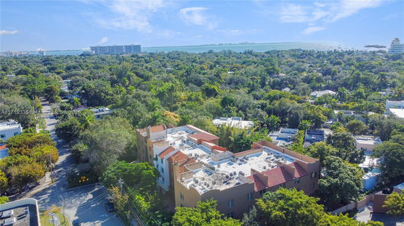 Aerial view overlooking a building with a flat rooftop surrounded by lush greenery and a distant view of the ocean.