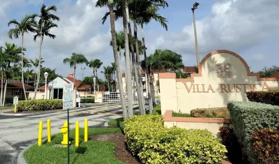 Entrance view of a residential complex named Villa Rustica with gated access and landscaped surroundings.