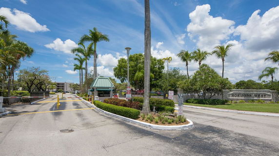 Entrance to a residential area with a small guard house and palm trees.