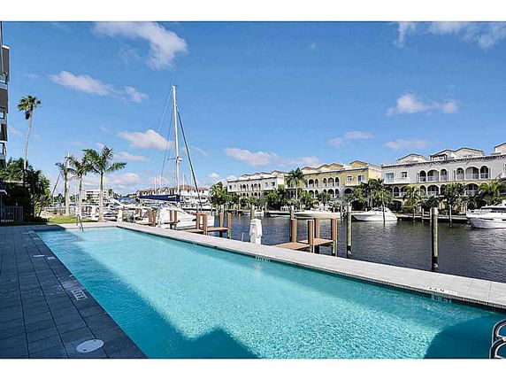 Outdoor swimming pool overlooking a marina with boats and multi-story buildings in the background.