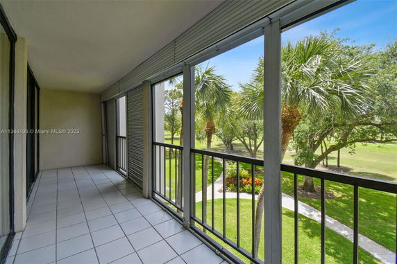 Balcony with tile flooring and a view of palm trees and a grassy area.