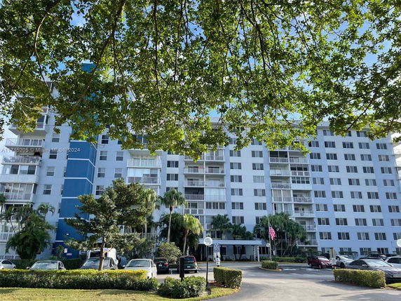 Front view of a multi-story residential building with balconies and a parking area in front.