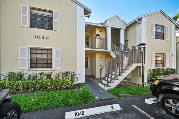 Front view of a two-story beige apartment building with white shutters and a stairway leading to the upper level.