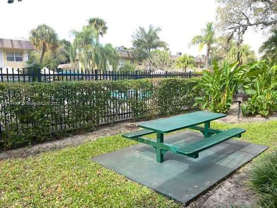 Outdoor area with a green picnic table near a fenced swimming pool.