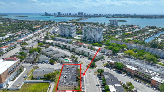 Aerial view of a residential area with a highlighted building, surrounded by water and distant city skyline.