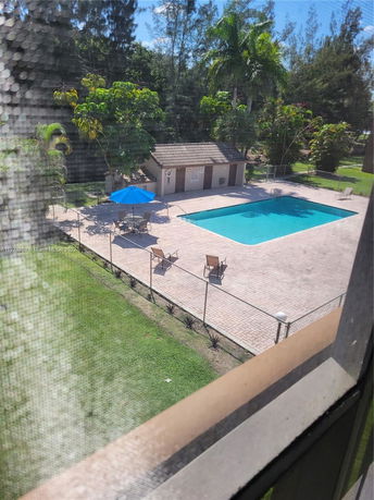 View of a swimming pool area with a small building nearby, surrounded by greenery.