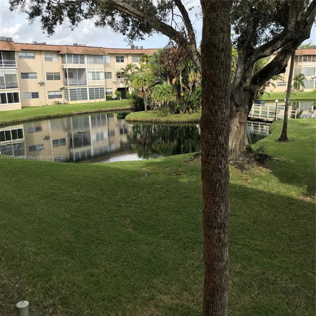 View of a pond with trees and residential buildings in the background.