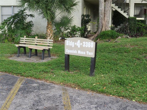 Outdoor view with a building sign and a bench, surrounded by grass and trees.
