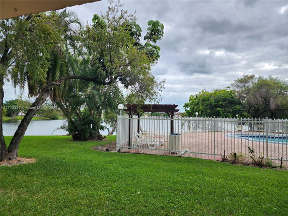 Outdoor swimming pool with a surrounding fence and nearby trees overlooking a body of water.