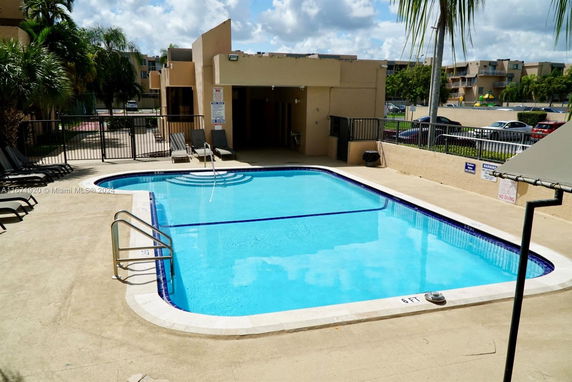 Outdoor swimming pool area with lounge chairs and a building in the background.