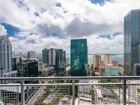 Cityscape view from a high-rise building balcony, showcasing multiple skyscrapers and water in the distance.