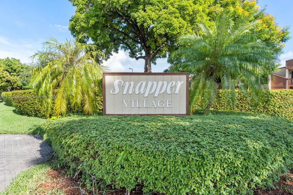 Outdoor sign for Snapper Village surrounded by greenery and trees.