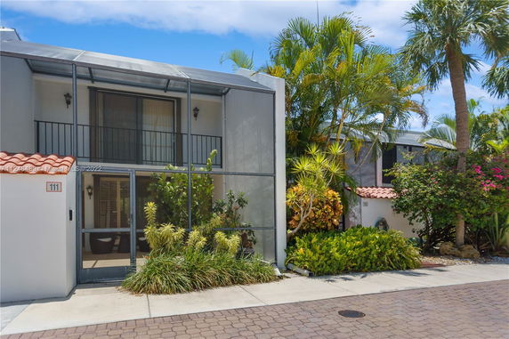 Front view of a house with a screened balcony and lush greenery.
