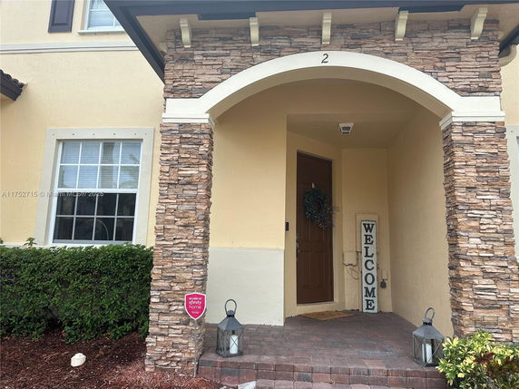 Front view of a house entrance with stone columns and a brown door.