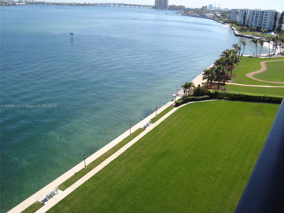 View overlooking a waterfront area with lush greenery and a walkway alongside the water.