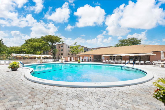 Outdoor view of a swimming pool with adjacent building and seating area.