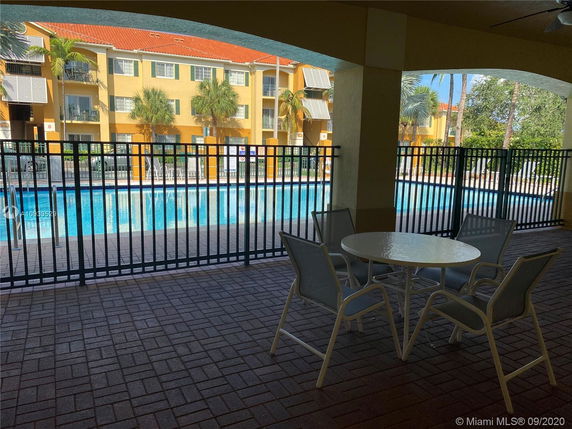 View of a swimming pool area with chairs and a table under an archway.