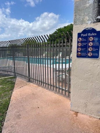 Gated entrance to a pool area with a sign displaying pool rules.