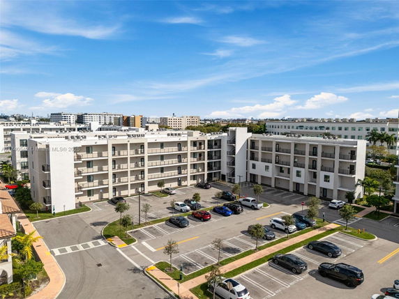 Front view of a multi-story residential building with balconies and a parking area in front.