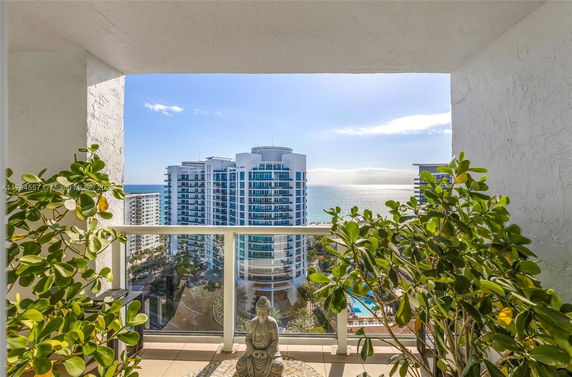 Panoramic view from a building balcony showing a coastal cityscape, including a modern high-rise and the ocean.