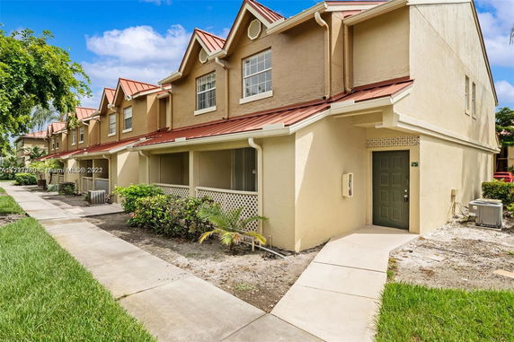Front view of a two-story townhouse with red roofing and beige exterior.