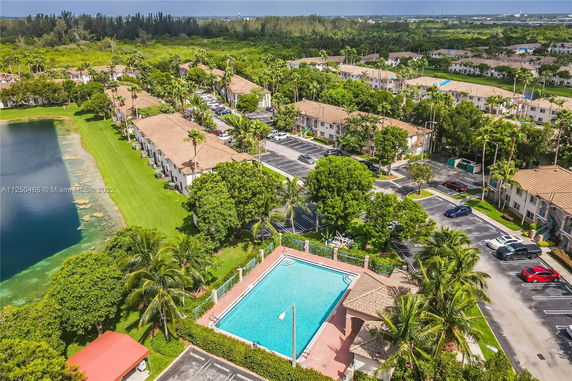 Aerial view of a residential area with apartment buildings, parking lots, a swimming pool, and a nearby lake.