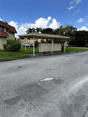 Covered parking area with a simple roof structure in front of buildings.