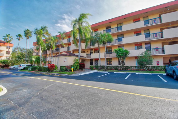 Front view of a multi-story building with balconies and a parking area.