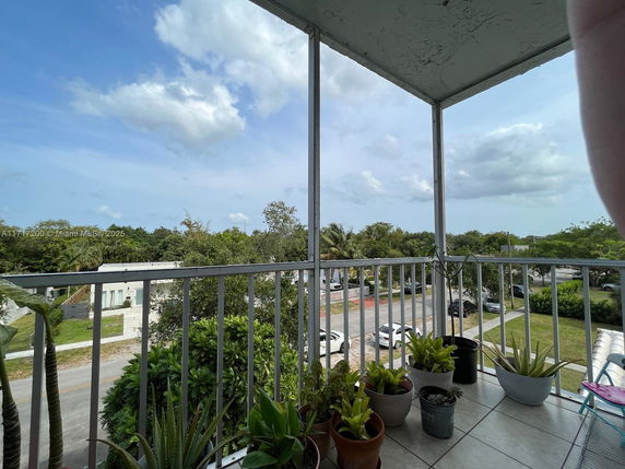 Panoramic view from a balcony with a railing and potted plants overlooking trees and a road.