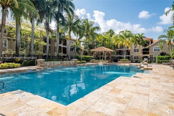 Outdoor swimming pool area with surrounding buildings and palm trees.