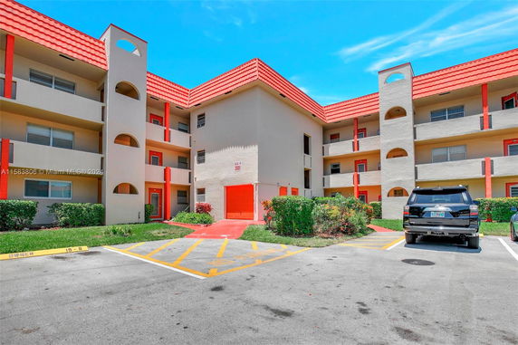 Front view of a multi-story building with red accents and parking spaces.