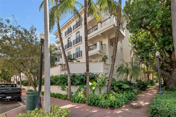 Front view of a multi-story building with multiple balconies and surrounded by tropical plants.