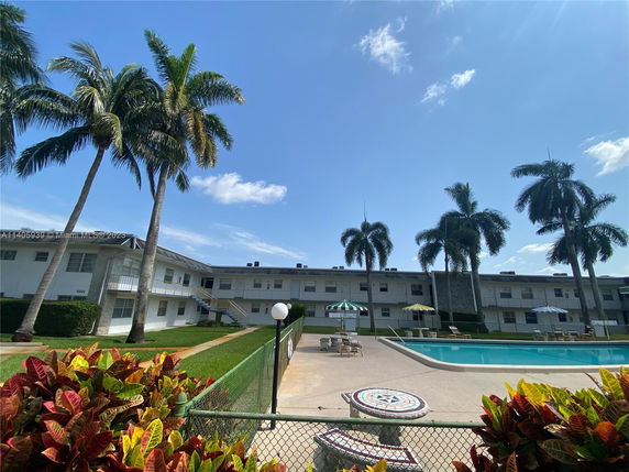 Outdoor view of a residential building with a swimming pool and surrounding palm trees.