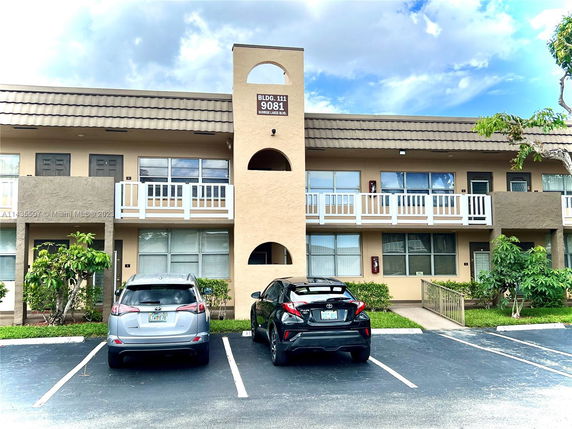 Front view of a two-story building with balconies and a parking area in front.