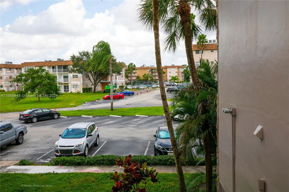View of a parking lot with multiple parked cars and apartment buildings in the background.
